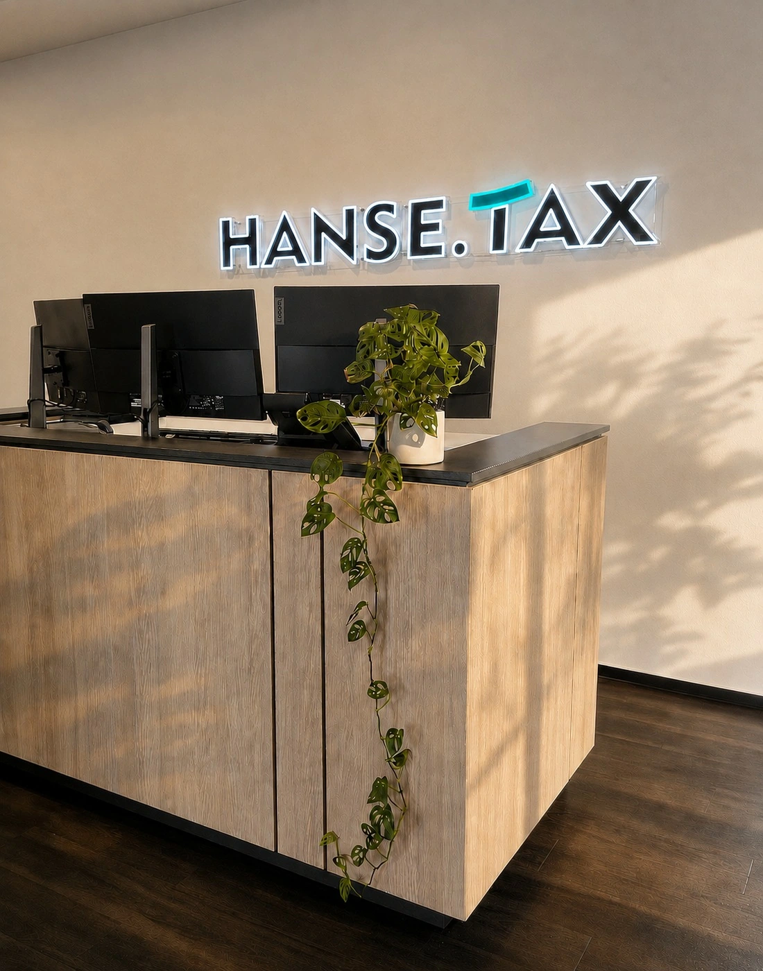 Empfangsbereich der Steuerberatungskanzlei HANSE.TAX in Hamburg mit Empfangstresen, Grünpflanze und beleuchtetem HANSE.TAX-Logo